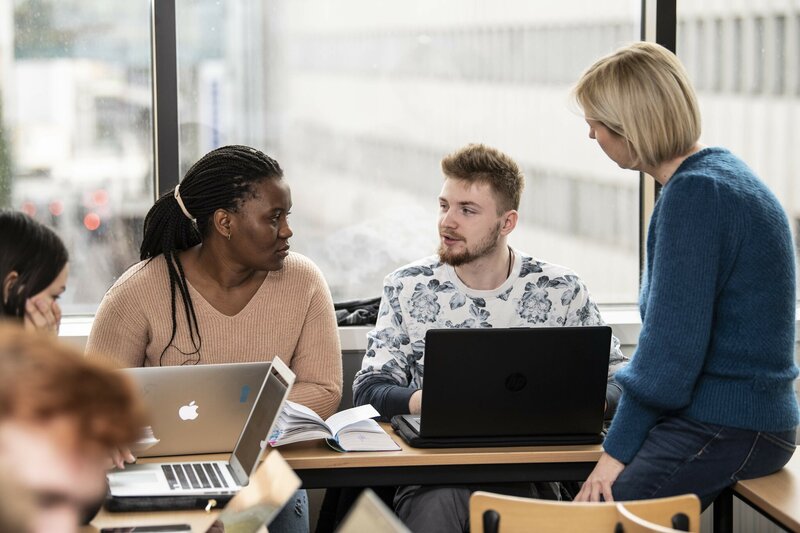 studenten werken samen achter laptop een docent staat hen bij